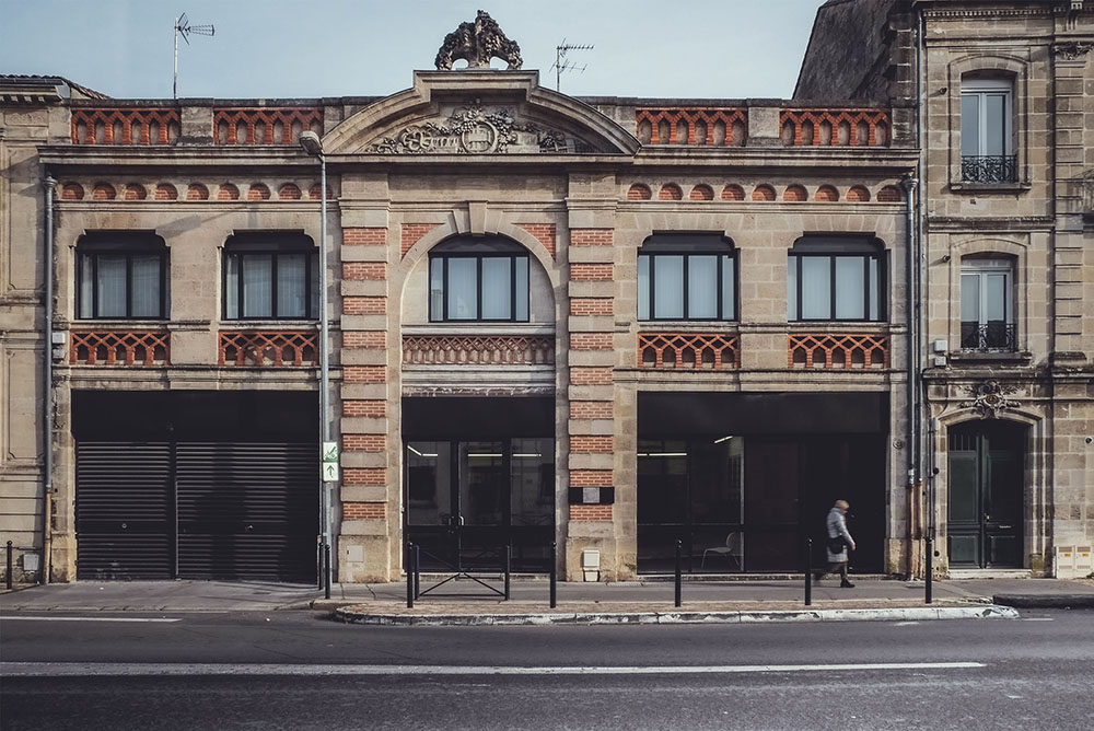 La façade de la galerie au 45 cours du Médoc : un ancien bâtiment commercial en pierre et brique, avec fronton sculpté.
