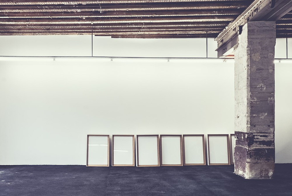 Un mur blanc avant l’accrochage, les cadres posés au sol.