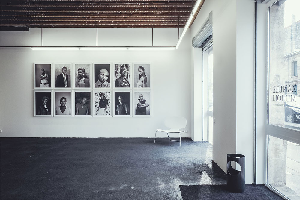 Une salle d’exposition : douze portraits en noir et blanc accrochés en deux rangées.