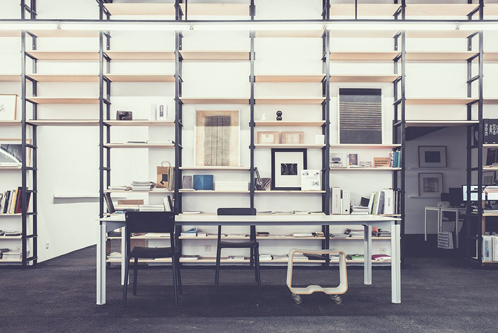 La bibliothèque : étagères métalliques, livres, grande table de travail.